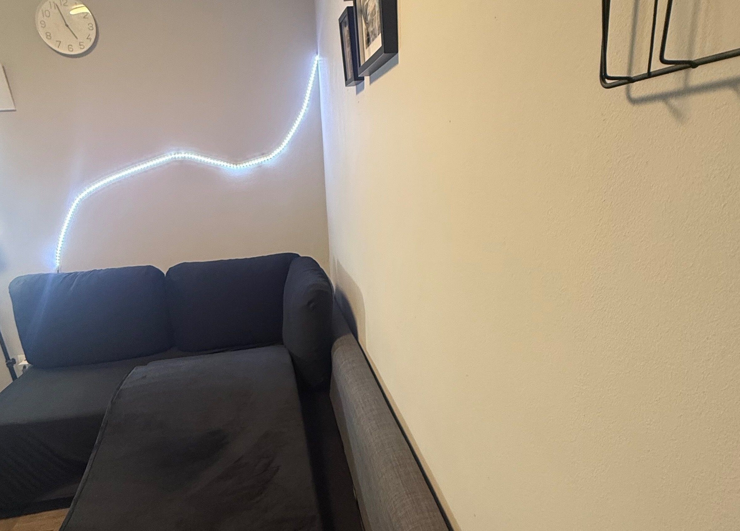 Sala acogedora en Kyiscejas, Barcelona, Catalunya, ES, con sofá negro y luz LED ambiental en la pared.