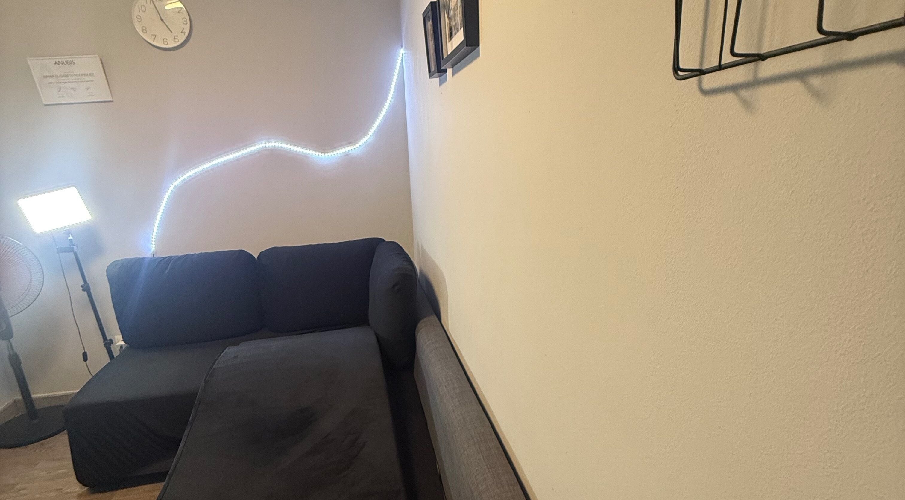 Sala acogedora en Kyiscejas, Barcelona, Catalunya, ES, con sofá negro y luz LED ambiental en la pared.