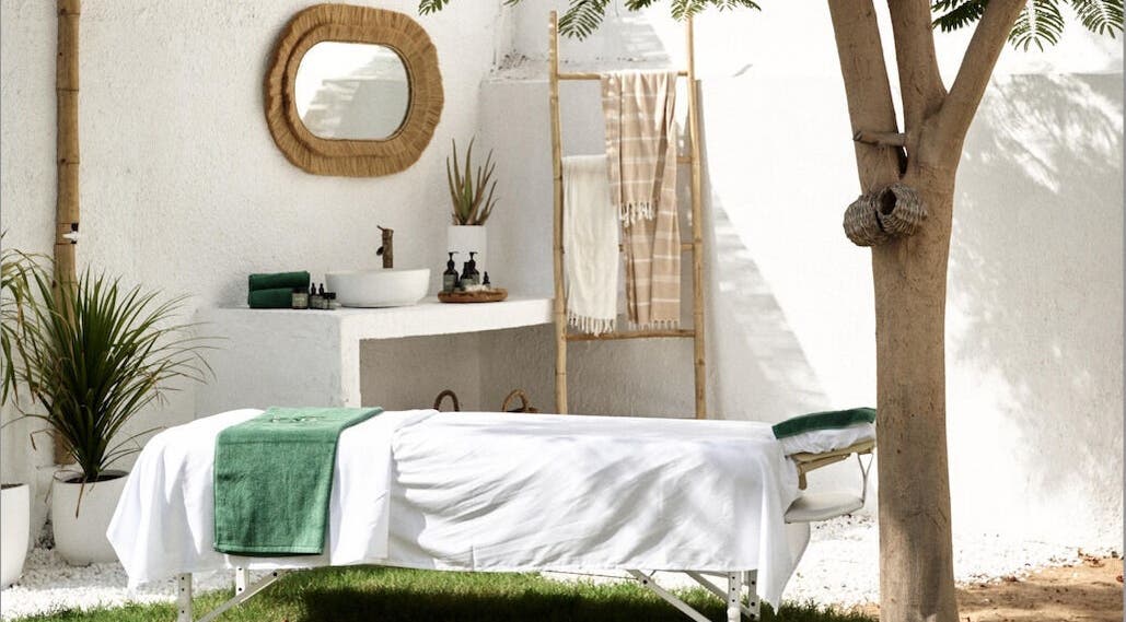 Outdoor massage setup at Raaha Wellness - Home Service, Dubai, AE, with green towel and tranquil surroundings.