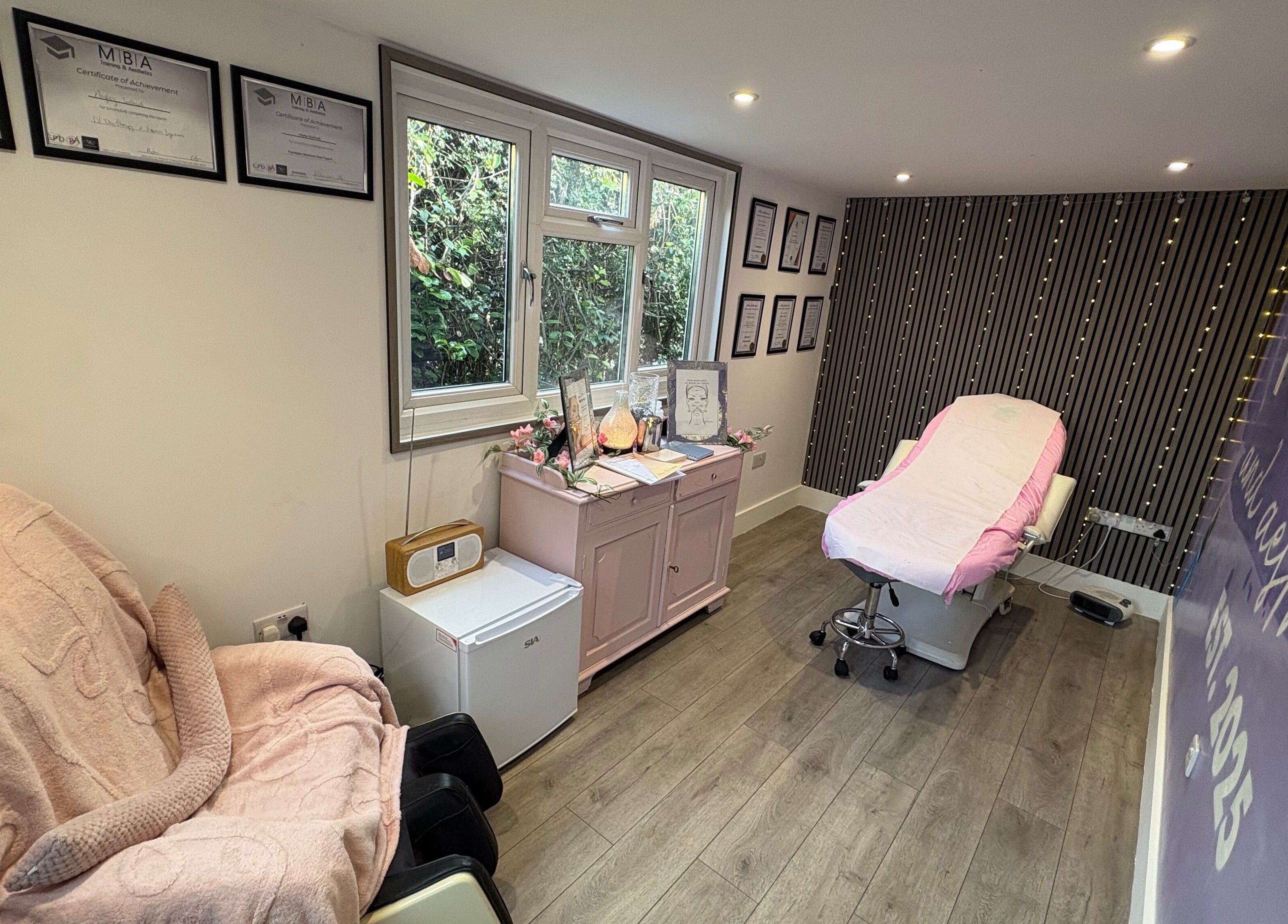 Relaxing treatment room at Pure IV and Aesthetics, Sarisbury Green, England, GB, with pink accents and certificates.