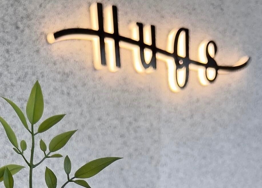 Warmly lit Hugs Beauty Salon sign with greenery, located in Muscat, Muscat Governorate, OM.