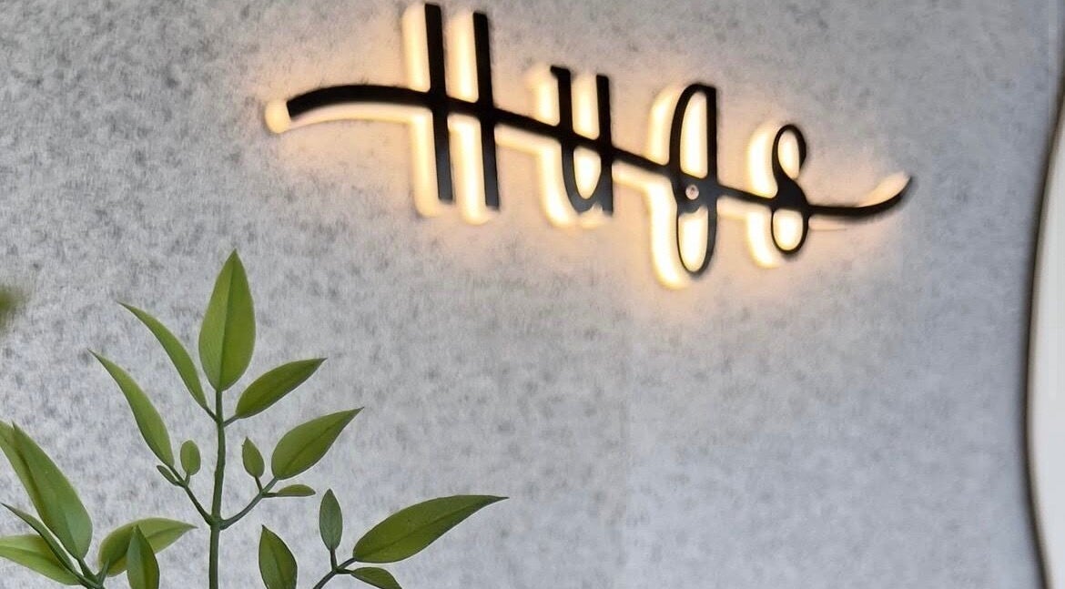 Warmly lit Hugs Beauty Salon sign with greenery, located in Muscat, Muscat Governorate, OM.