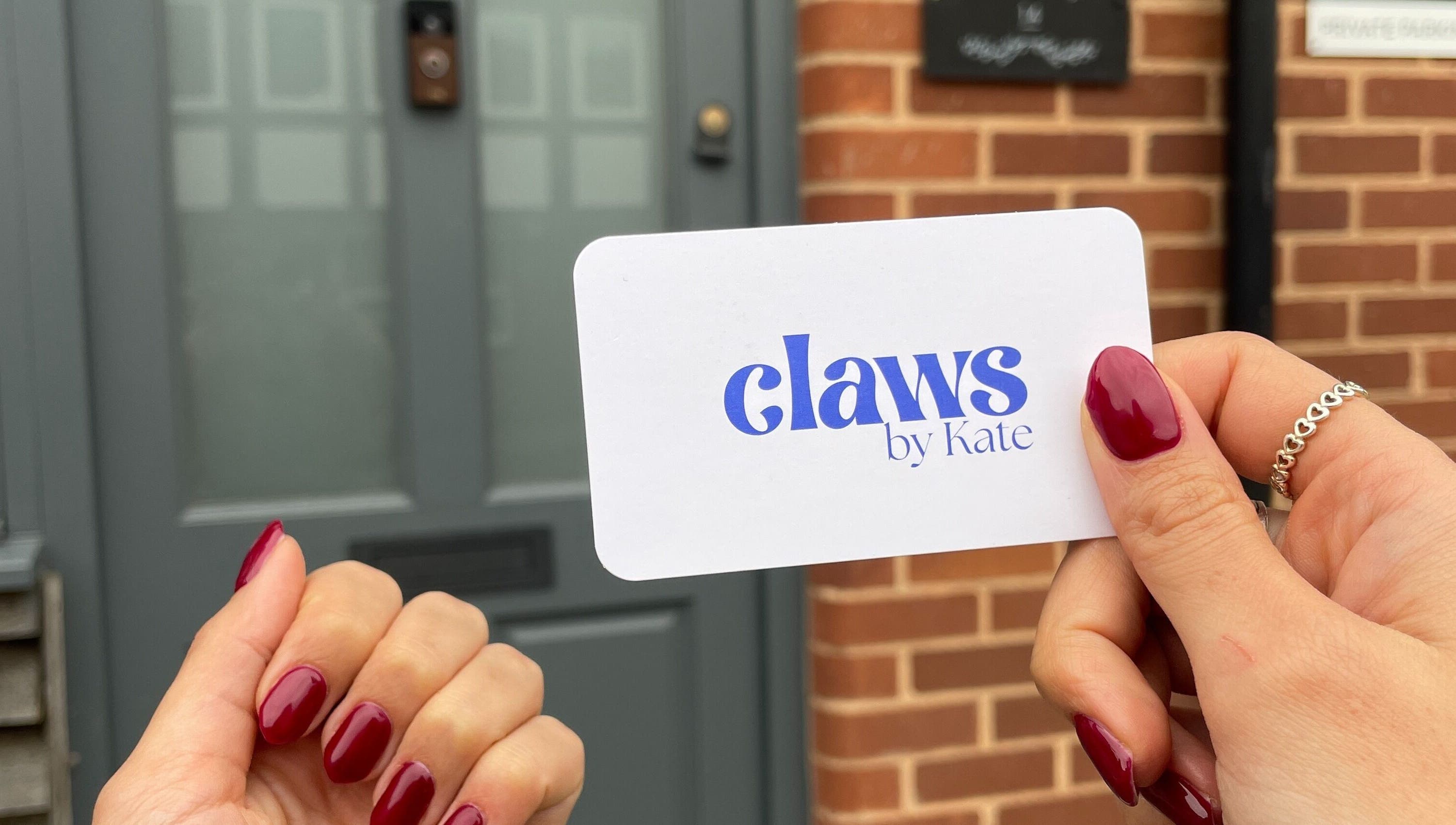 Hand with red nails holding Claws By Kate card at Knowle, England, GB entrance.