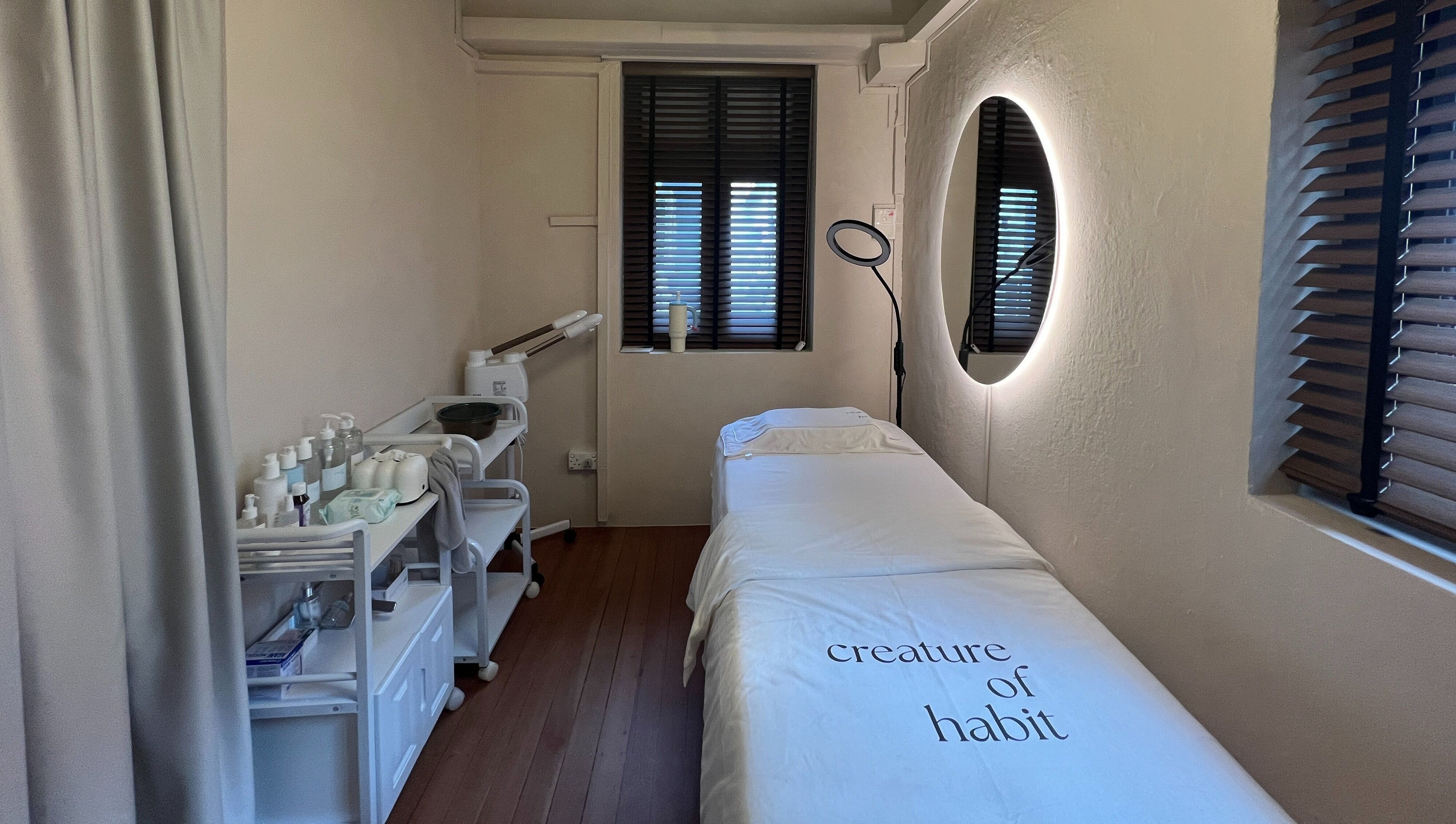 Tranquil spa room at Creature Of Habit, Singapore, SG showcasing a cozy treatment bed and products.