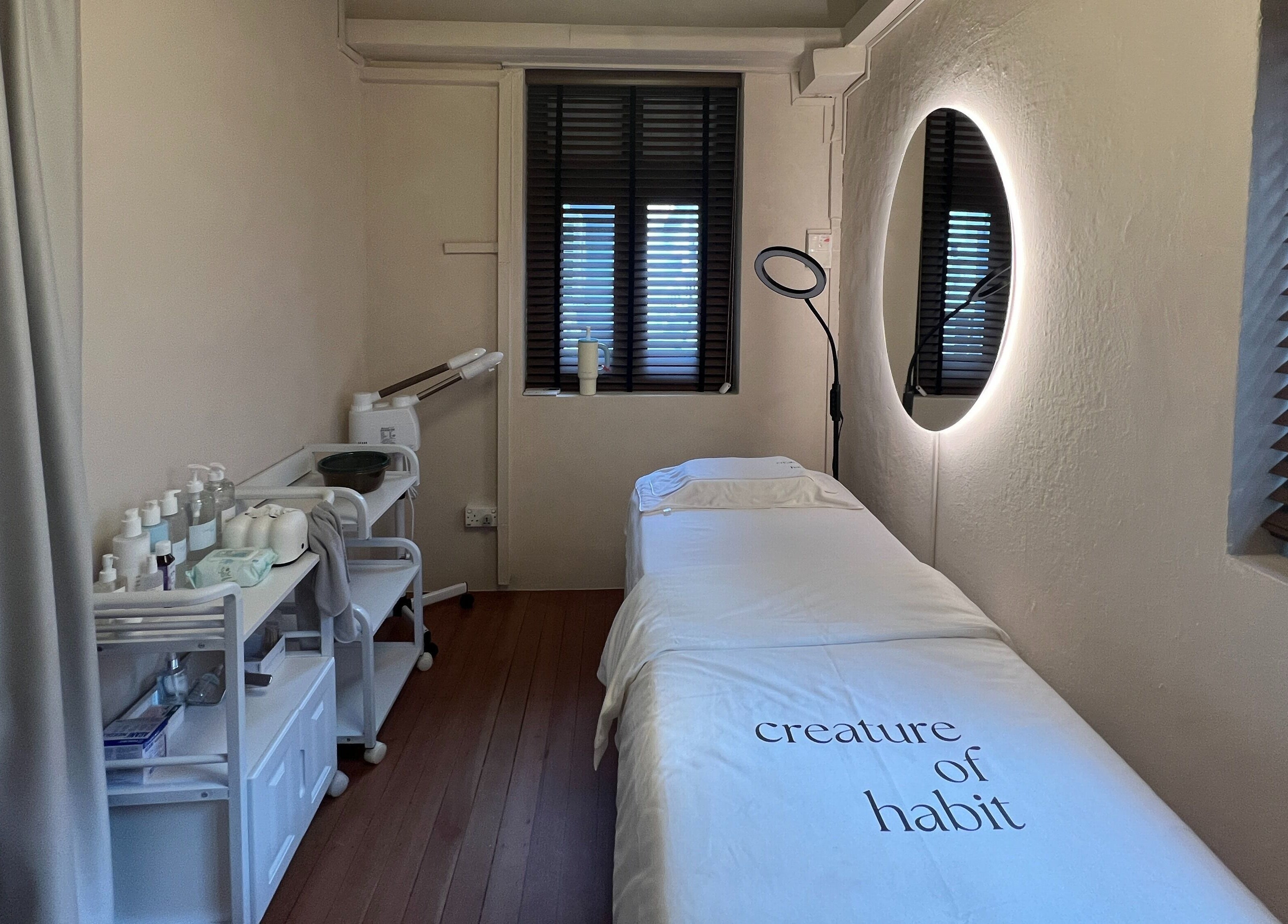 Tranquil spa room at Creature Of Habit, Singapore, SG showcasing a cozy treatment bed and products.