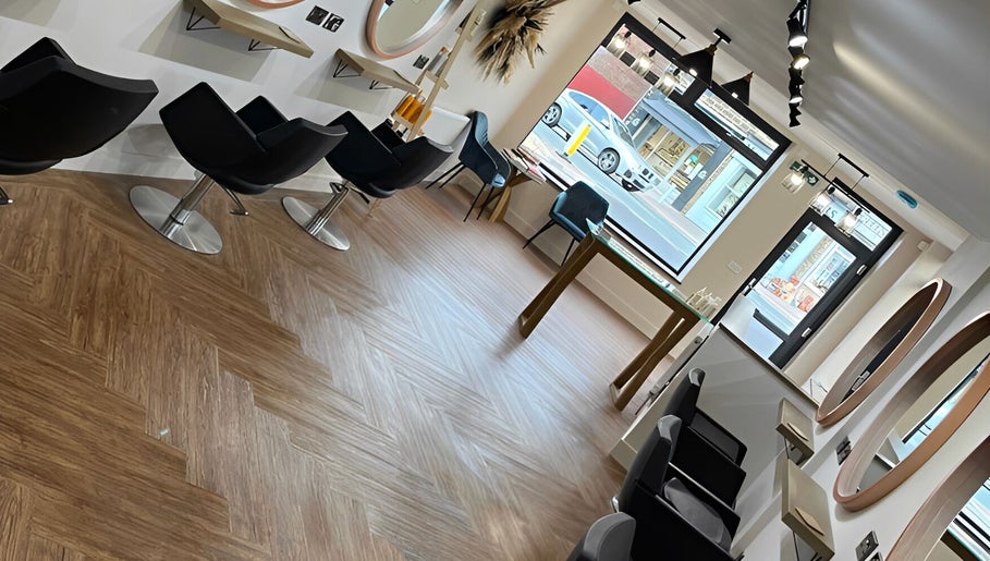 Stylish hair salon interior at HairByHM at Chique in Mapplewell, England, GB with sleek black chairs and mirrors.