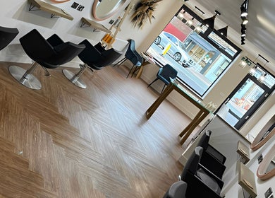 Stylish hair salon interior at HairByHM at Chique in Mapplewell, England, GB with sleek black chairs and mirrors.