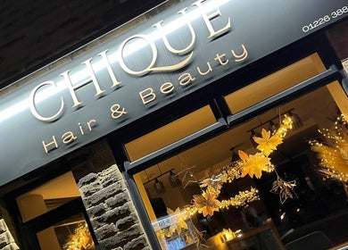 Exterior view of HairByHM at Chique in Mapplewell, England, GB with illuminated sign and elegant decor.