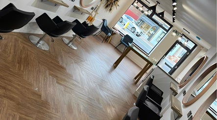 Modern salon interior at Hair By HM at Chique, Mapplewell, England, GB with sleek black chairs and wood flooring.
