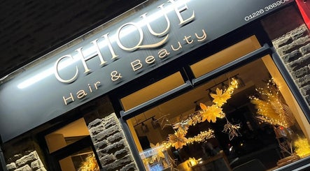 Front view of Hair By HM at Chique in Mapplewell, England, GB, showcasing its illuminated signage.