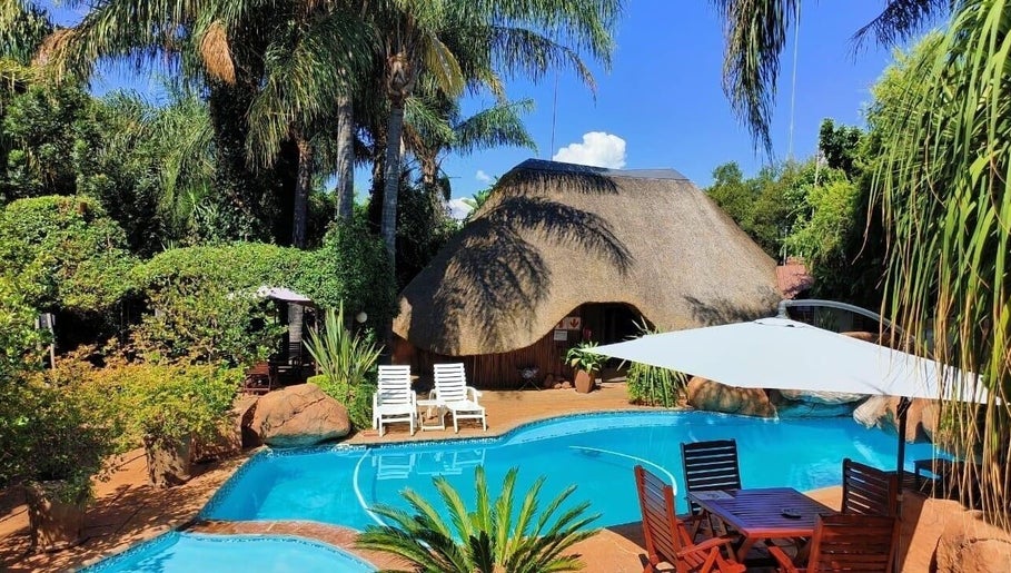 Outdoor pool at Francor Guesthouse & Spa in Akasia, Gauteng, ZA, surrounded by lush greenery and thatched roof.