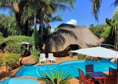 Outdoor pool at Francor Guesthouse & Spa in Akasia, Gauteng, ZA, surrounded by lush greenery and thatched roof.