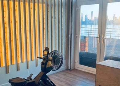 Bright fitness room at Wellbeing with Lucy in Birkenhead, England, GB, featuring a rowing machine and city view.