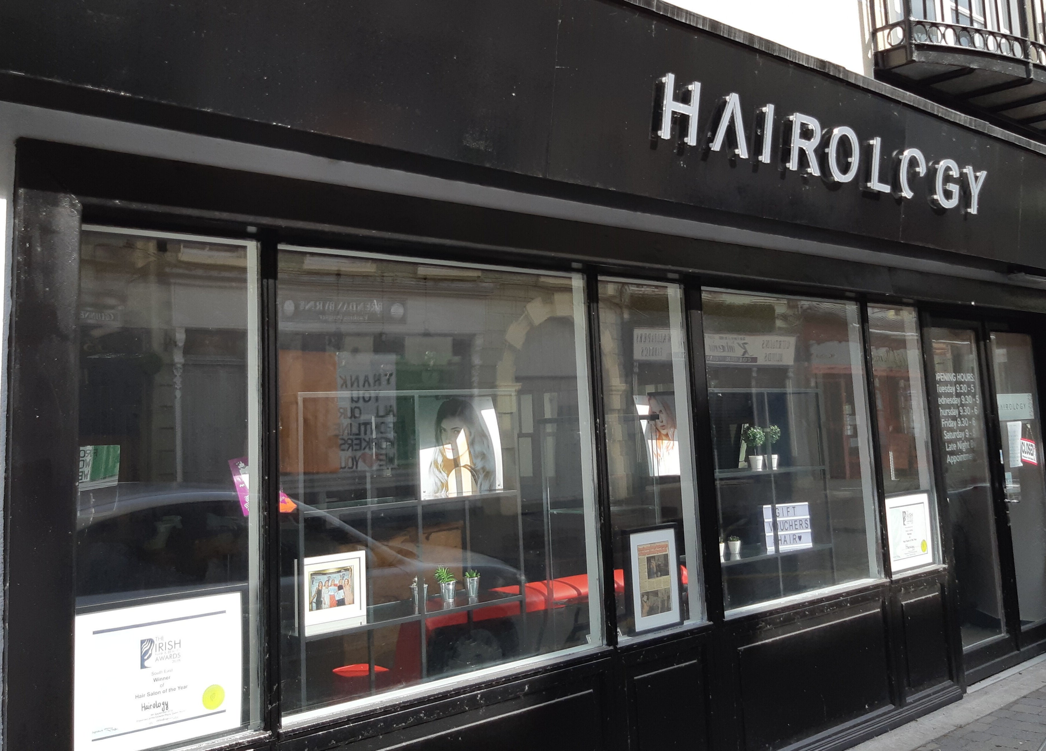 Street view of Hairology salon in Carlow, County Carlow, IE with modern black storefront and large glass windows.