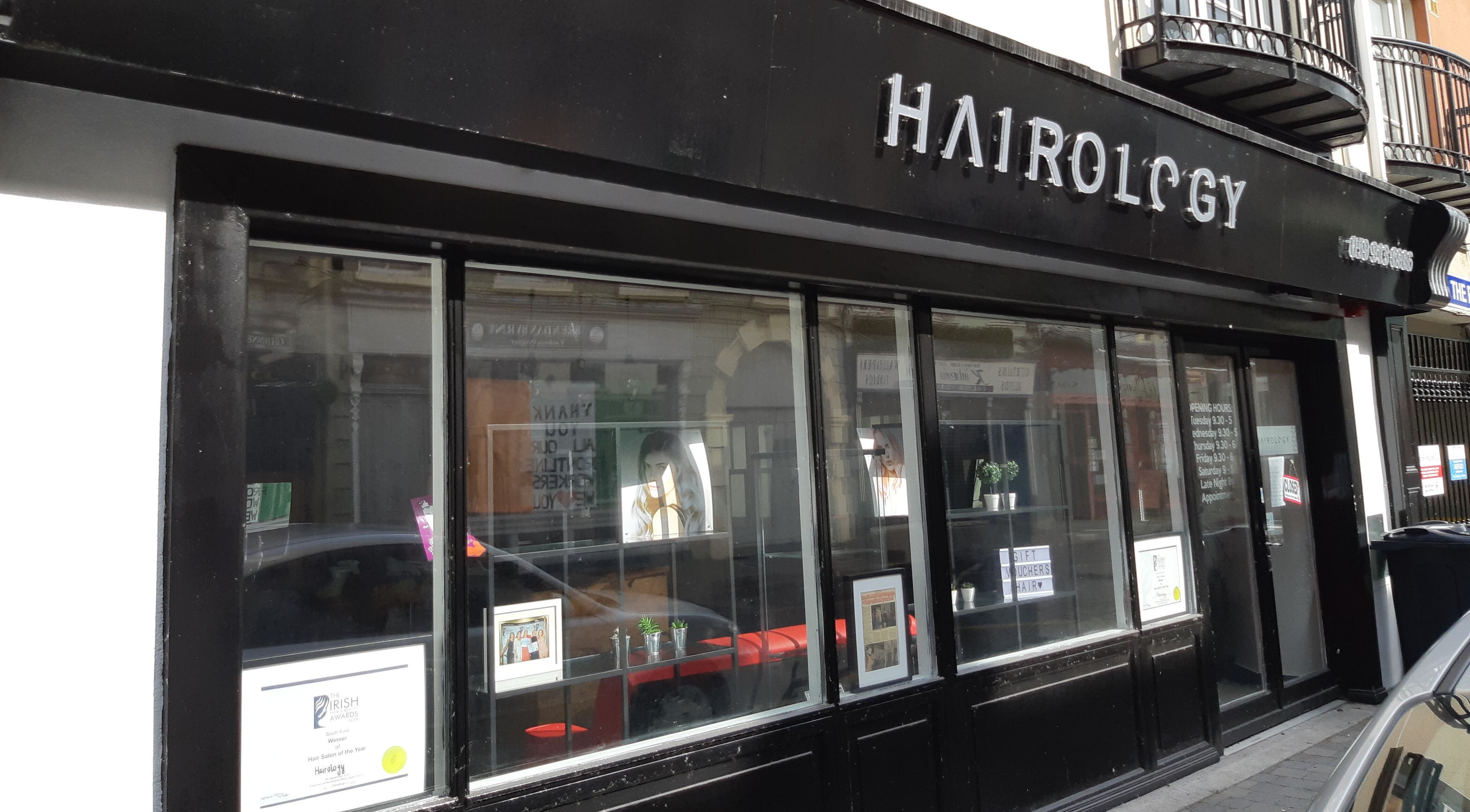 Street view of Hairology salon in Carlow, County Carlow, IE with modern black storefront and large glass windows.