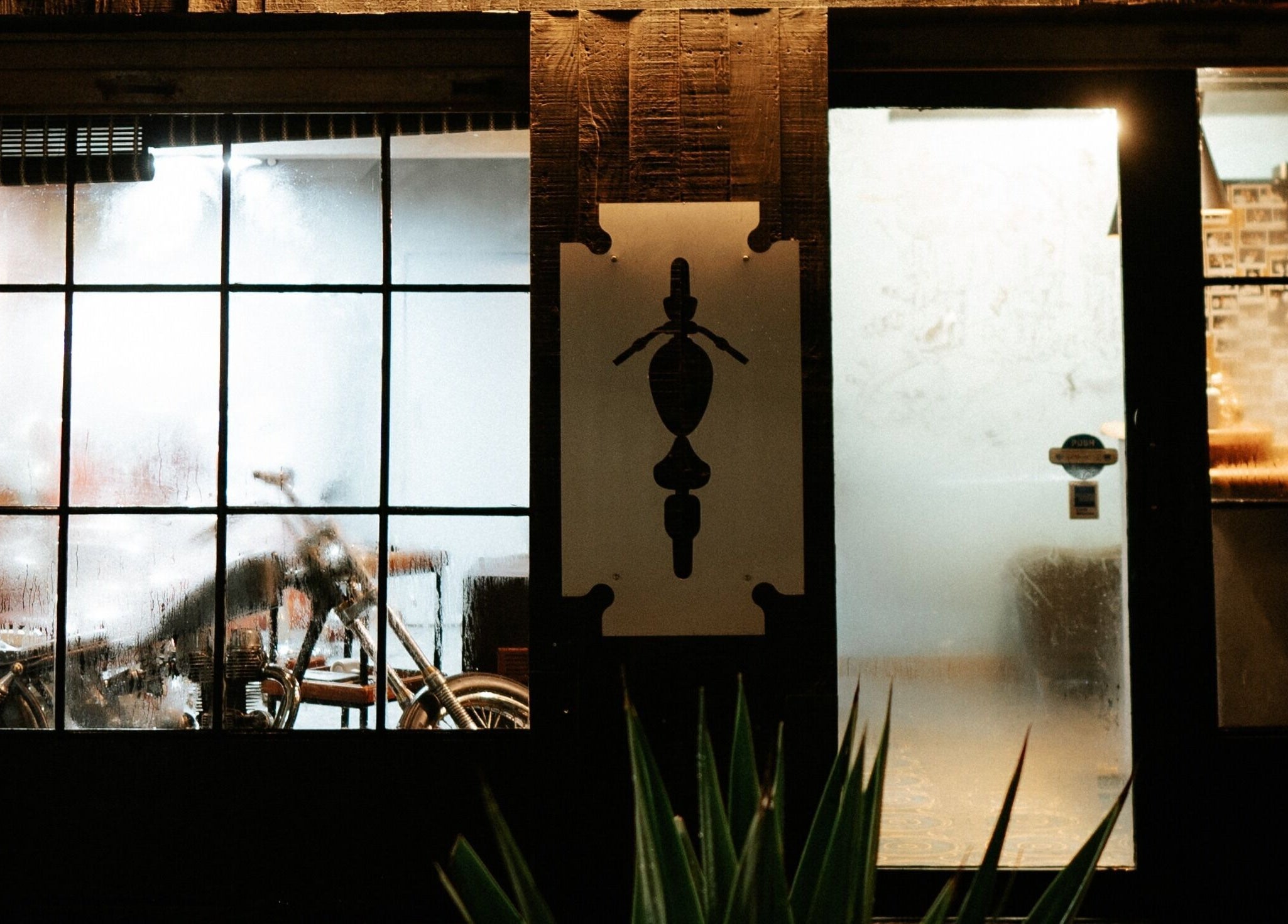 Steamy glass window of Goodfellas Barber & Brand | Est. 2018, Vagator, Goa, IN, revealing a motorcycle inside.