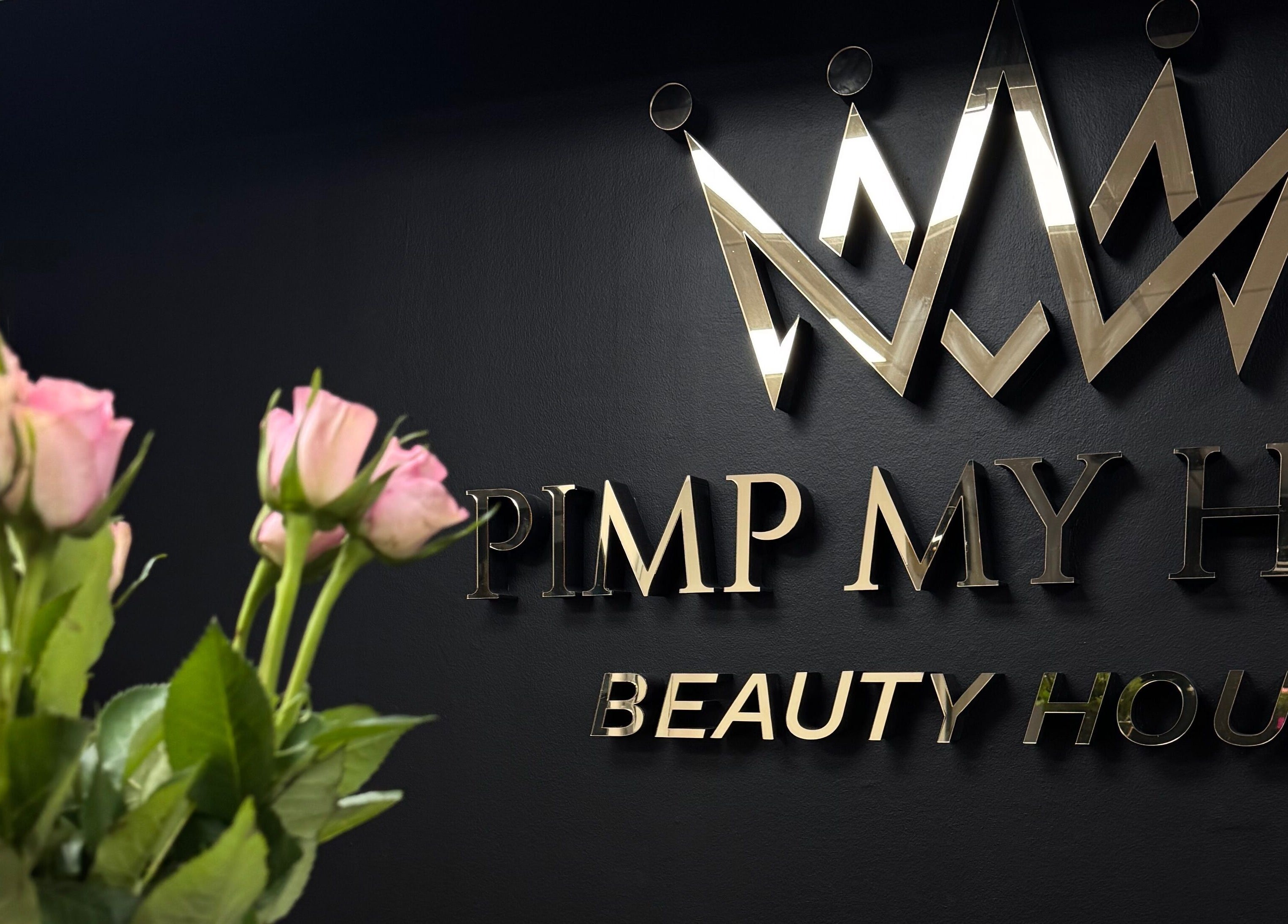 Stylish crown logo at Pimp My Hair in Aberdeen, Scotland, GB, with pink roses in the foreground.