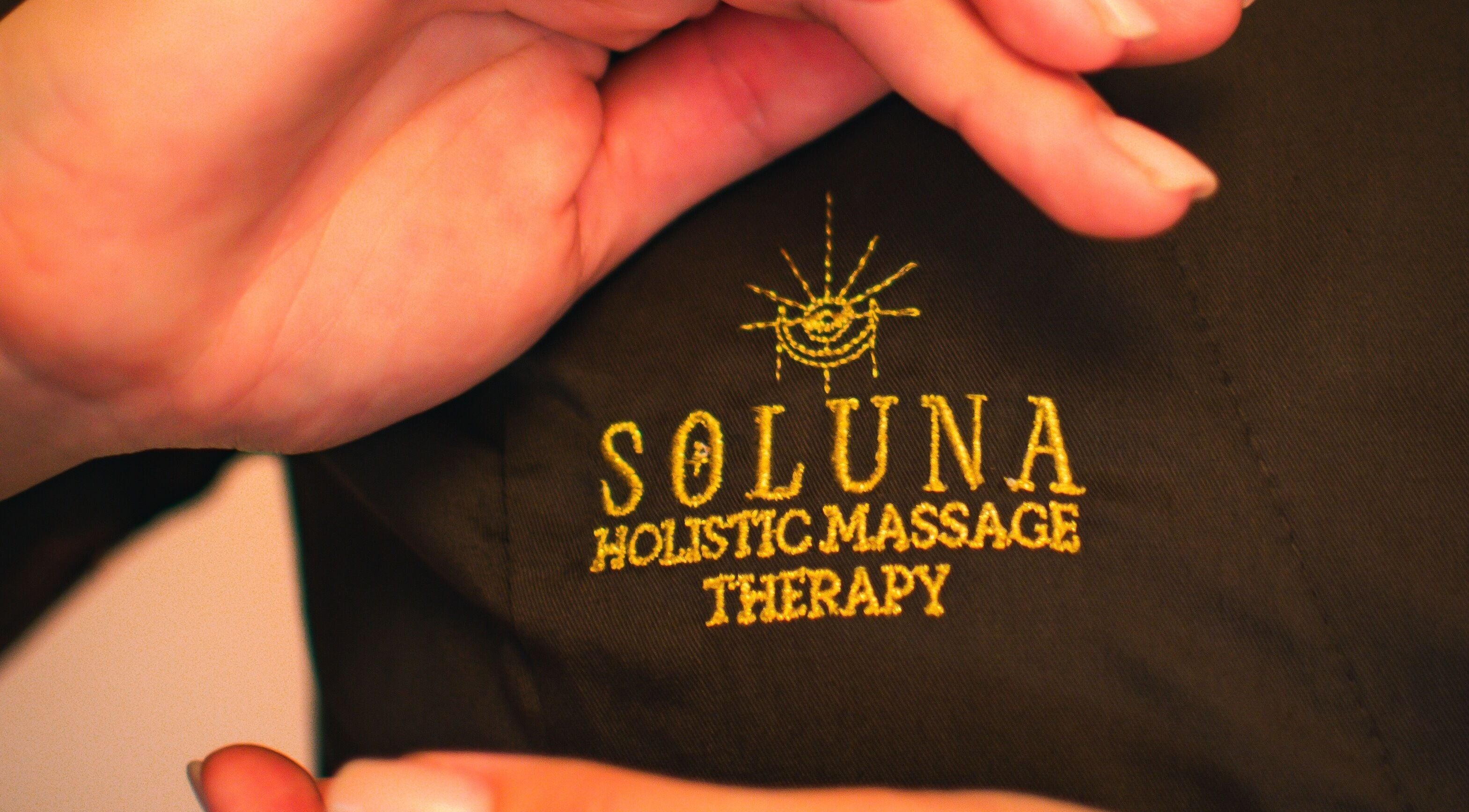 Close-up of the SOLUNA Holistic Massage Therapy logo on uniform in London, England, GB.