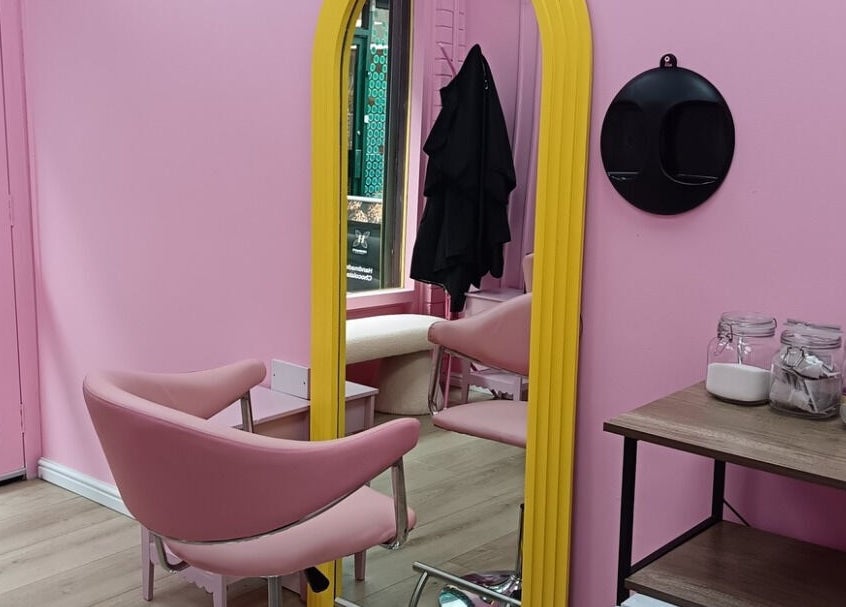 Chic pink interior at Franks salon, Cheadle, England, GB with stylish seating and decorative jars on shelf.