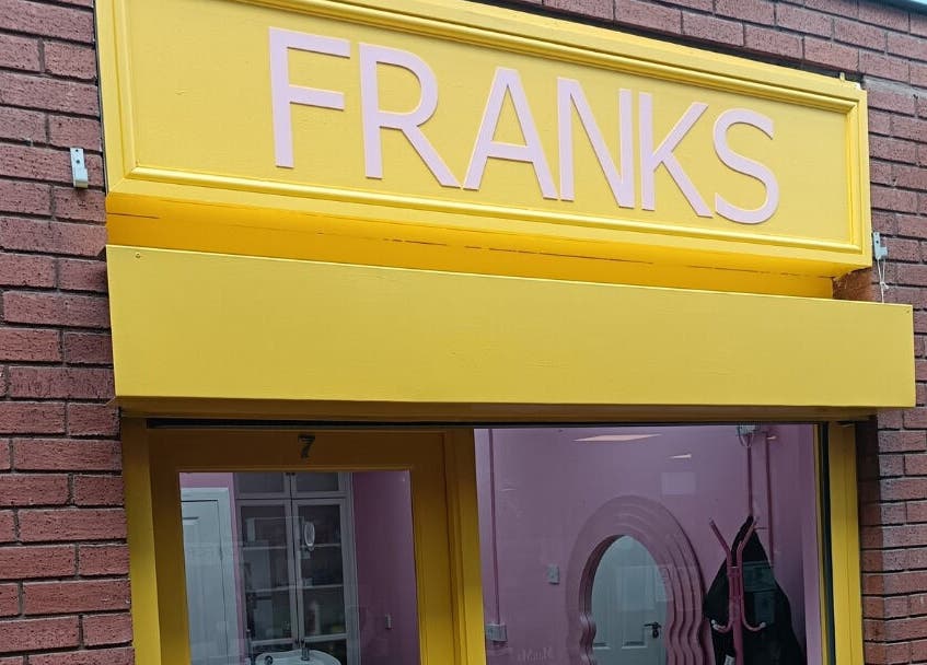 Bright yellow facade of Franks beauty salon in Cheadle, England, GB, featuring sleek signage.