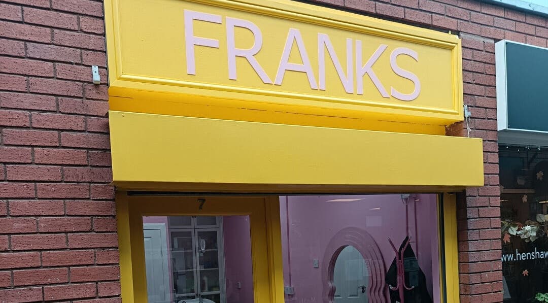 Bright yellow facade of Franks beauty salon in Cheadle, England, GB, featuring sleek signage.