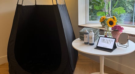 Tanning setup at Bronzed by Chlo, Manchester, England, GB with tent, products, and vibrant flowers.