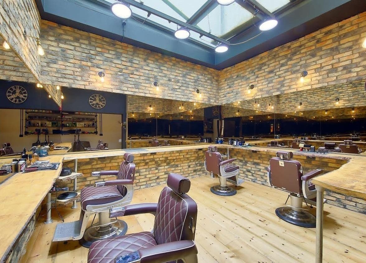 Spacious interior of The Dapper Fox - Wandsworth, showcasing modern barber chairs and rustic brick walls in London, England, GB.