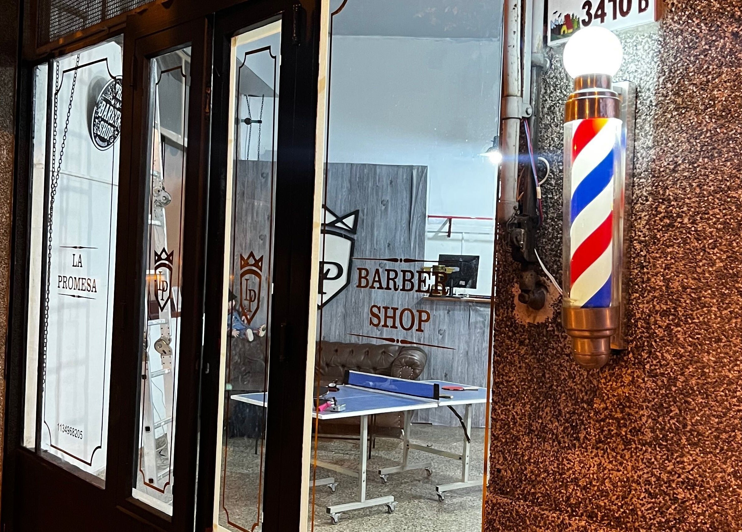 Entrada de La promesa SA, Villa San Andrés, Provincia De Buenos Aires, con cartel de barbería iluminado.