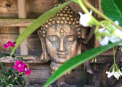 Buddha statue in garden at Bespoke Wellness & Academy, Dublin, County Dublin, IE surrounded by vibrant flowers.