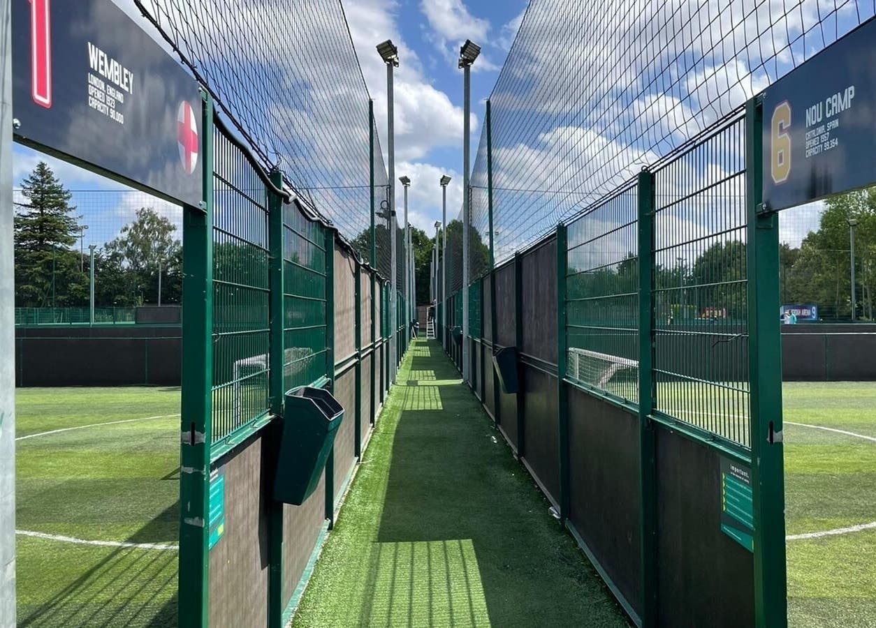 Enclosed soccer pitches at SW Football Academy, Tolworth, England, GB with lush green fields under a blue sky.