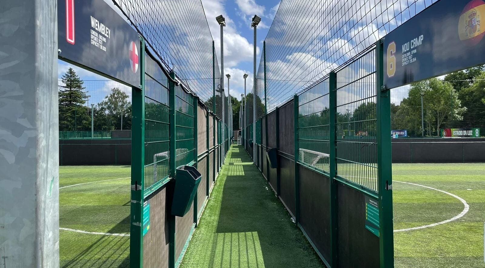 Enclosed soccer pitches at SW Football Academy, Tolworth, England, GB with lush green fields under a blue sky.