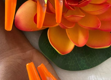 Mains avec ongles orange vif chez Flash Ongle Gigi, Sainte-rose, Basse-terre, GP, avec une fleur colorée.