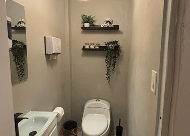 Baño elegante de Oasis Nails Spa en San Juan, PR, con decoración minimalista y plantas colgantes.