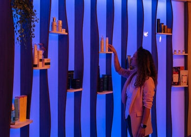 Mujer elige productos en una estantería iluminada en Cocoon’ink Wellness Studio, Mataró, Catalunya, ES.