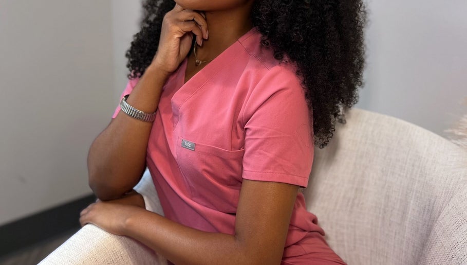 Alexis Lashae, Licensed Esthetician, sitting in a chair at Alpharetta, Georgia, US in a pink uniform.