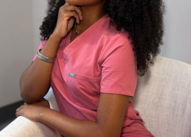 Alexis Lashae, Licensed Esthetician, sitting in a chair at Alpharetta, Georgia, US in a pink uniform.