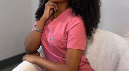 Alexis Lashae, Licensed Esthetician, sitting in a chair at Alpharetta, Georgia, US in a pink uniform.