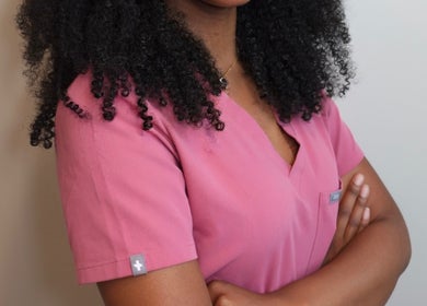 Alexis Lashae, Licensed Esthetician in Alpharetta, Georgia, wearing a pink uniform, arms folded confidently.