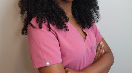 Alexis Lashae, Licensed Esthetician in Alpharetta, Georgia, wearing a pink uniform, arms folded confidently.