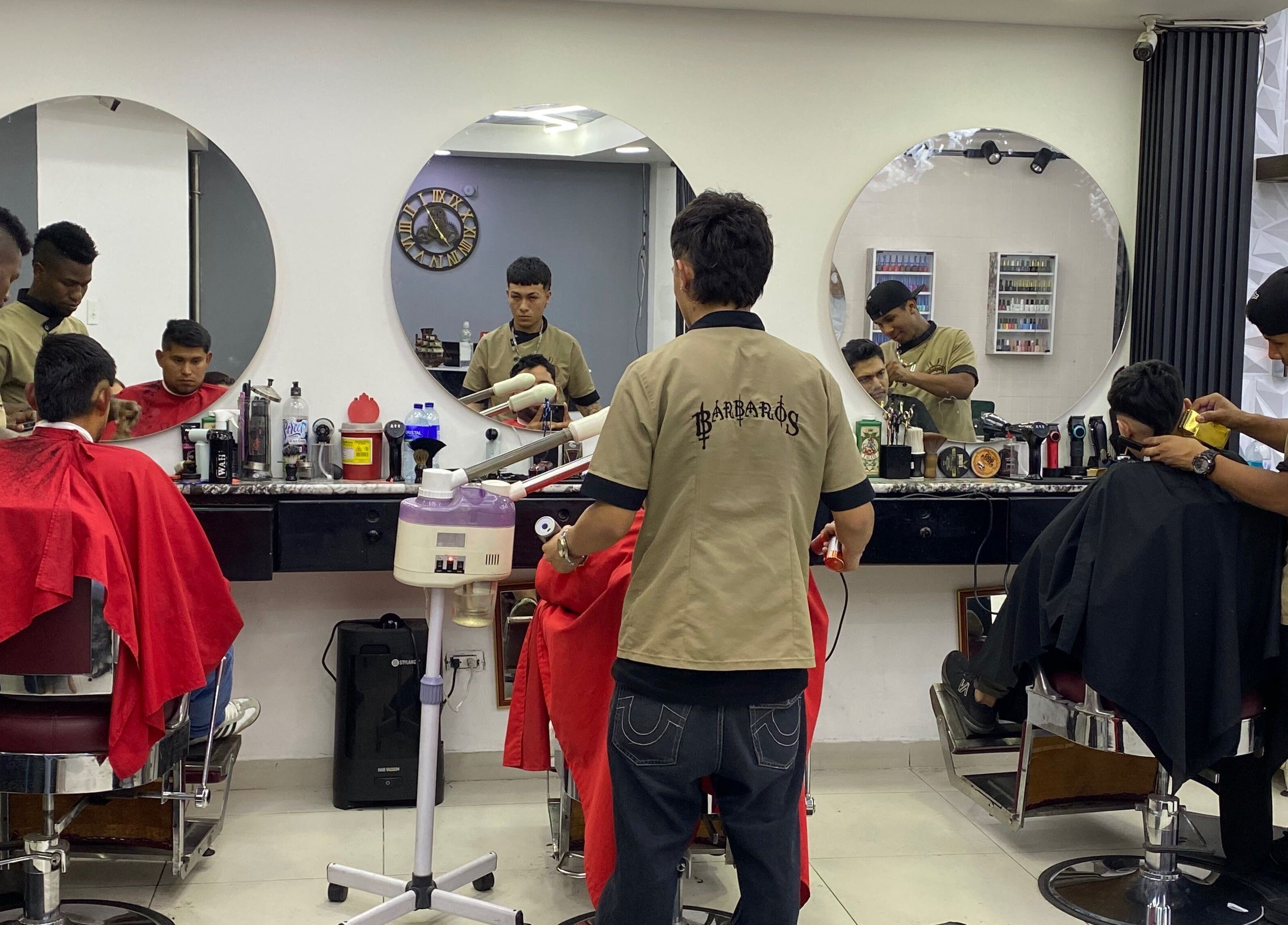 Estilistas de Q'Barbaros en Bogotá, CO, cortan cabello en un salón moderno con espejos redondos.
