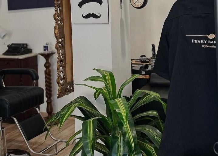 Interno del Peaky Barber Shop by Jonathan Di Tizio a Livorno, Toscana, IT, con arredi eleganti e pianta verde.