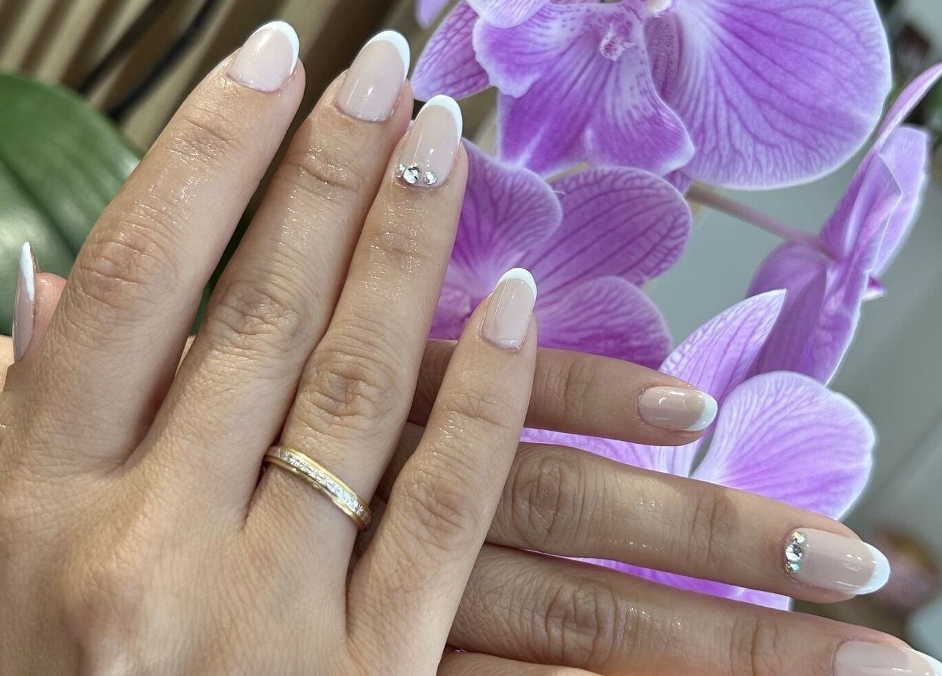 Uñas francesas decoradas en Clinic Nails, Vigo, ES, junto a una orquídea lila.