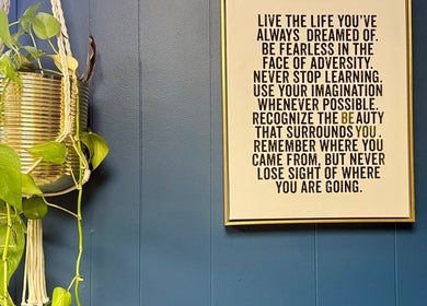Wall art and plant at Be Well Bozeman, Bozeman, Montana, US. Motivational quote framed beside greenery.