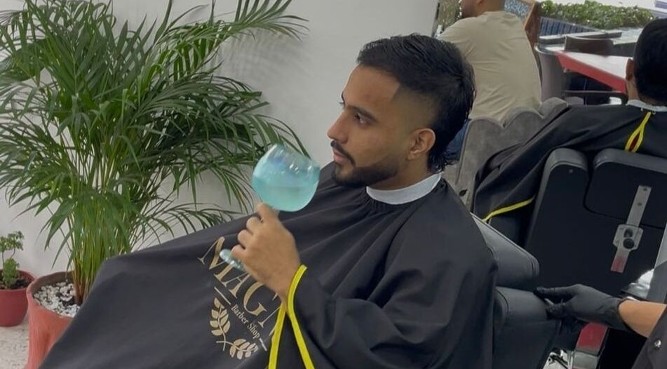 Cliente relajado en Magnus Barbershop, Cali, Valle Del Cauca, CO con cóctel en mano, rodeado de plantas.