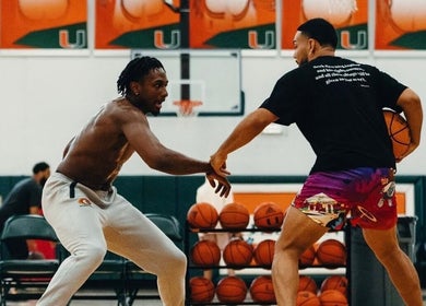 Two men playing basketball indoors at Winning Culture, Miami, Florida, US, surrounded by basketballs.