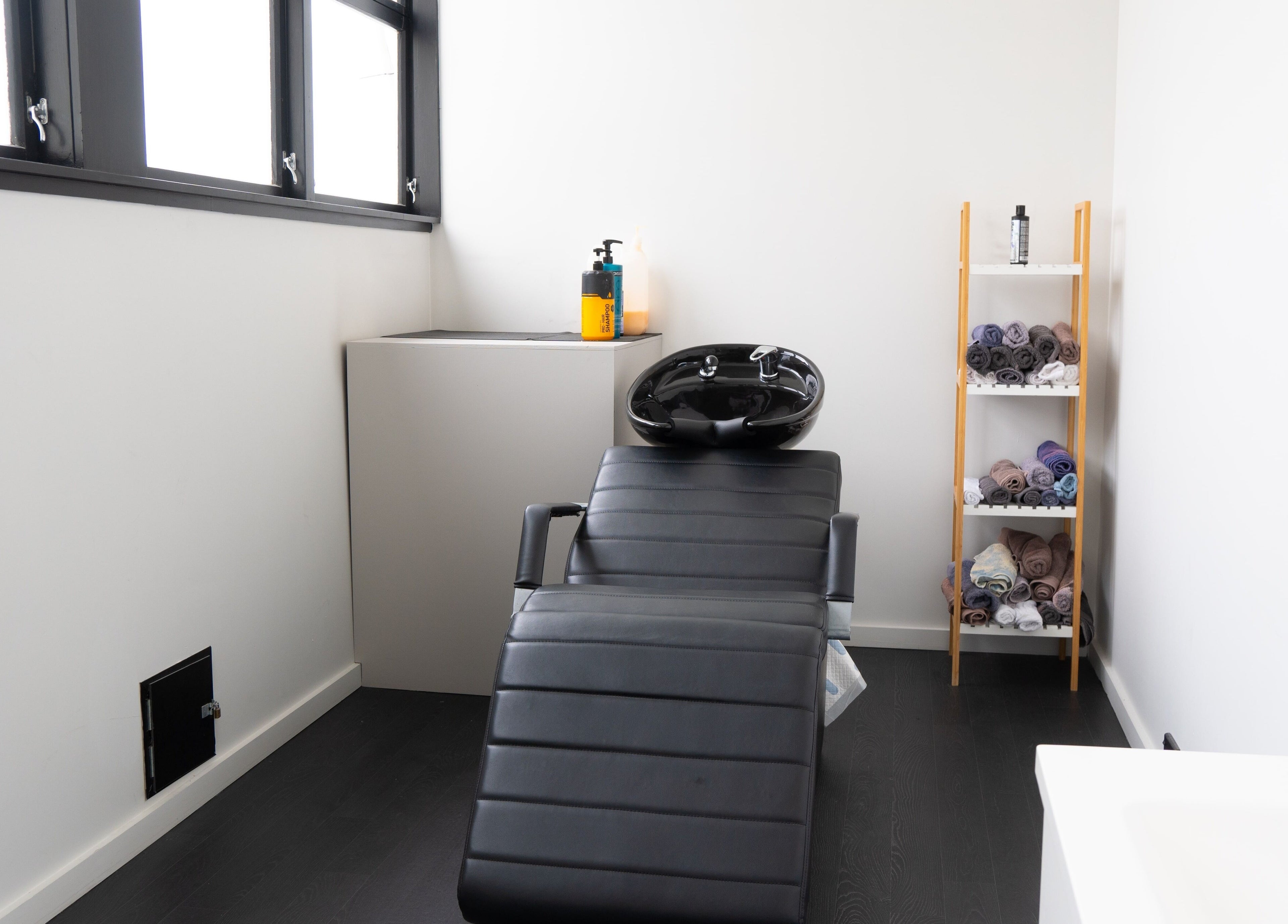 Modern wash station at Eight One Eight Barbershop, Auckland, NZ featuring stylish black leather chair and shelves with towels.