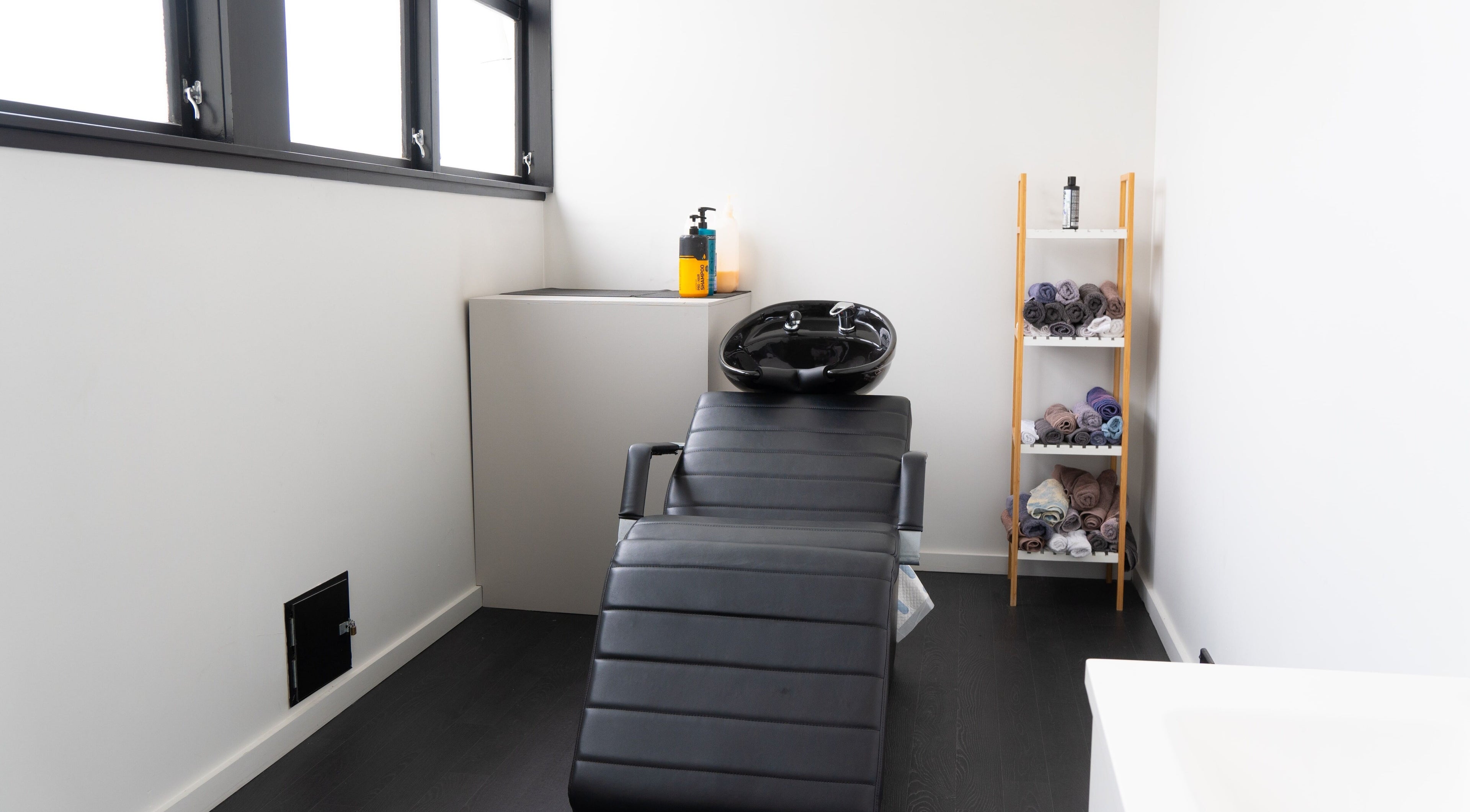 Modern wash station at Eight One Eight Barbershop, Auckland, NZ featuring stylish black leather chair and shelves with towels.