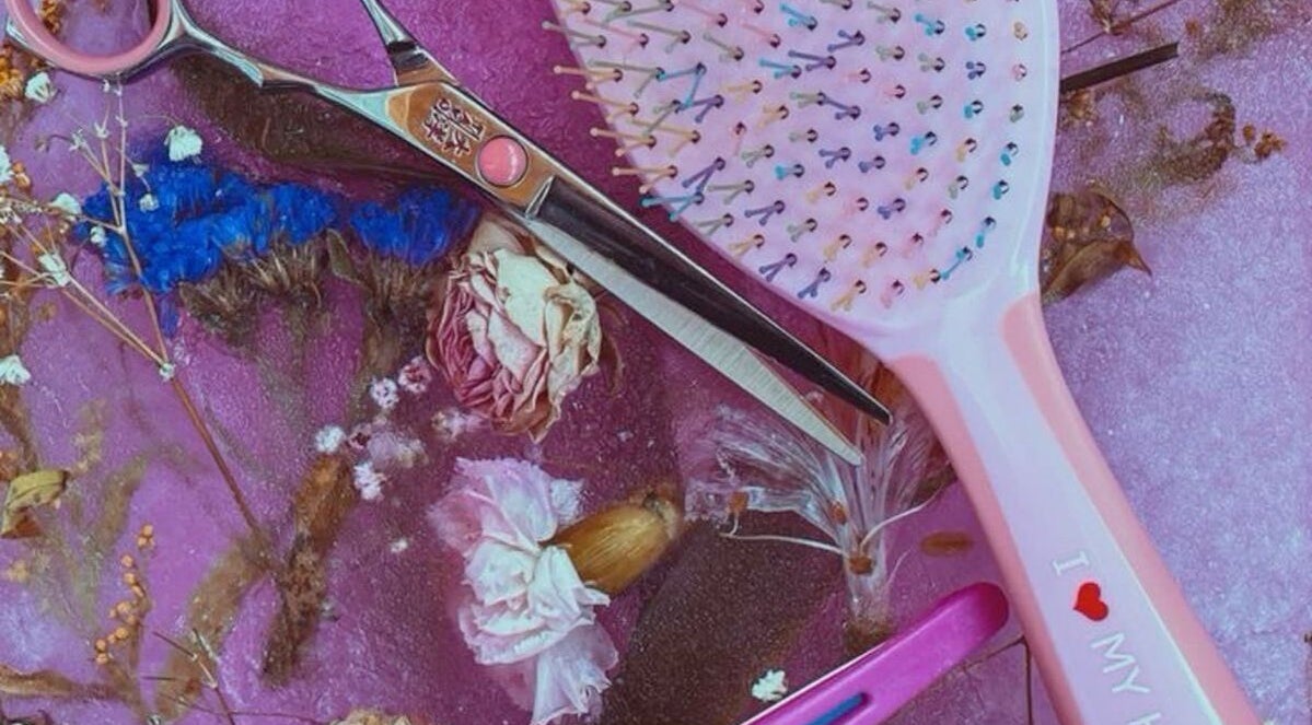 Colorful hairbrush and scissors on floral backdrop at 828_LuxBeauty, Manchester, Missouri, US.