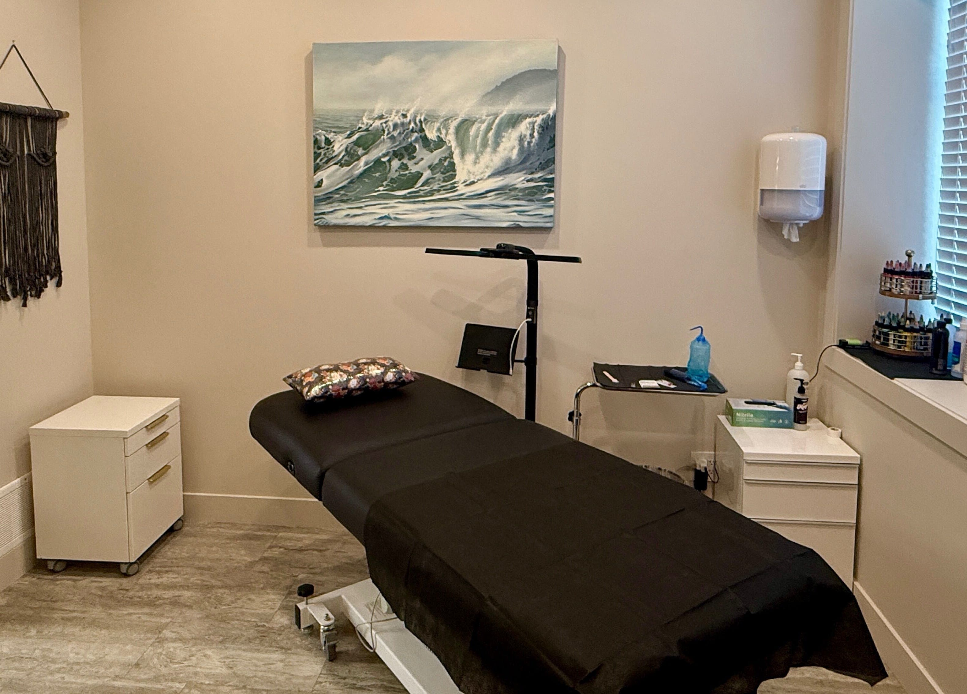 Calm treatment room at Jessie Grant - Ember Studio, Kelowna, British Columbia, CA with massage bed and ocean artwork.