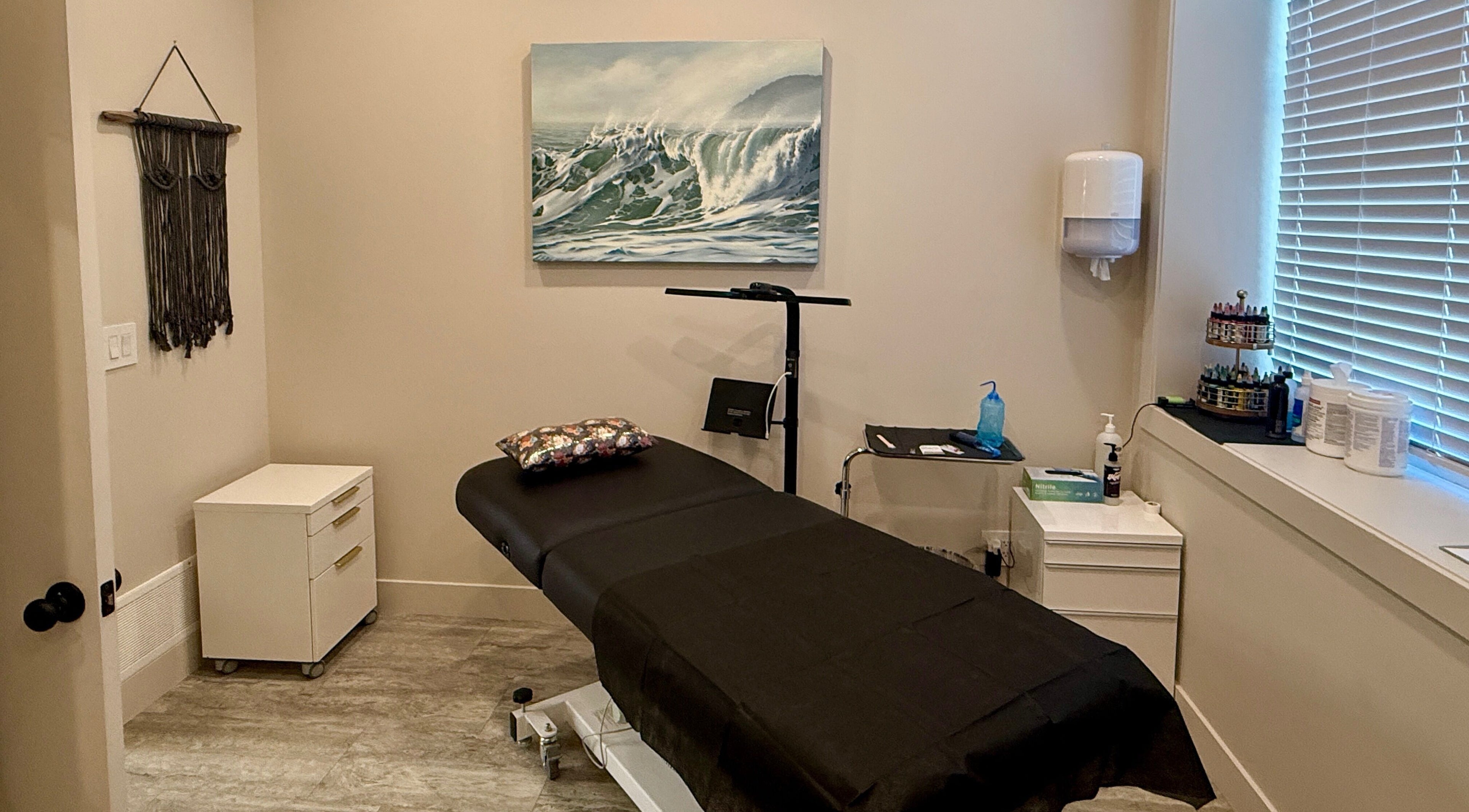 Calm treatment room at Jessie Grant - Ember Studio, Kelowna, British Columbia, CA with massage bed and ocean artwork.